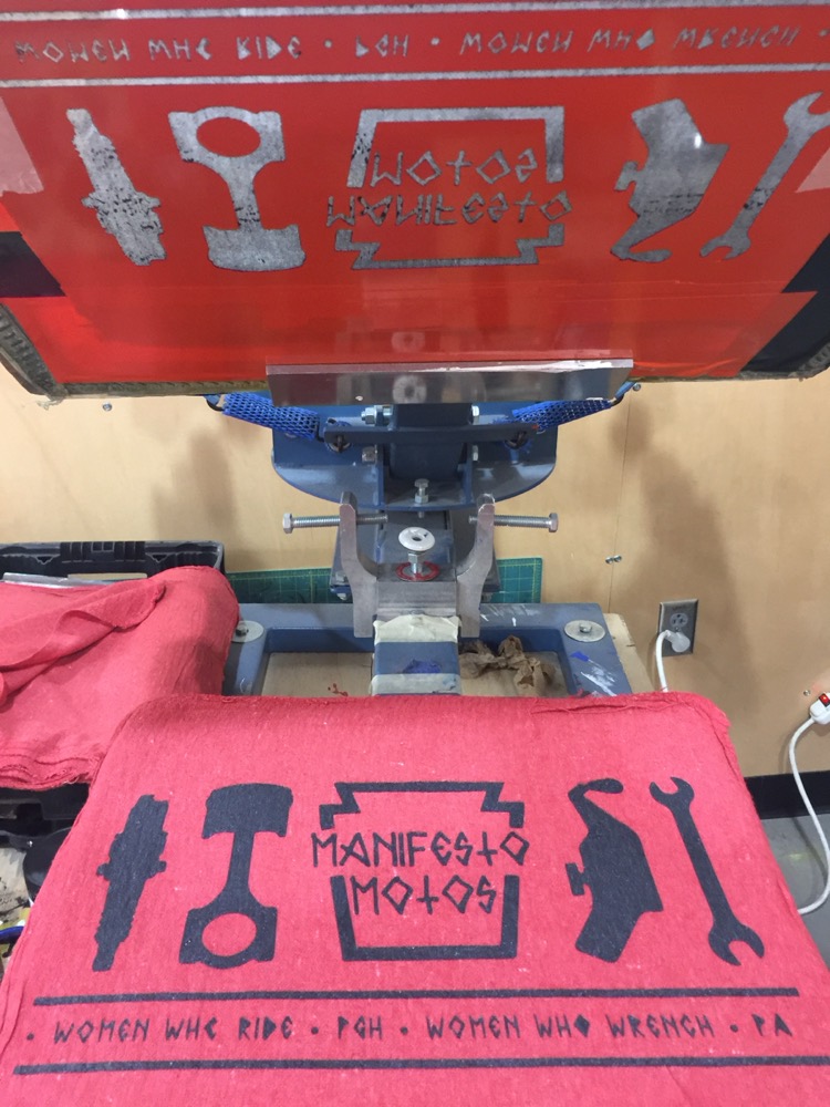 A screen-printed 'Manifesto Motos' shirt on a press.